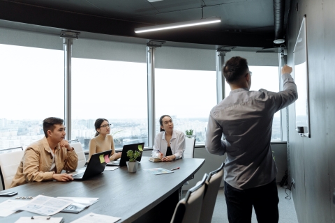 Person pointing at white board while colleagues look on