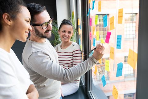 Employees writing on sticky notes on window at development session